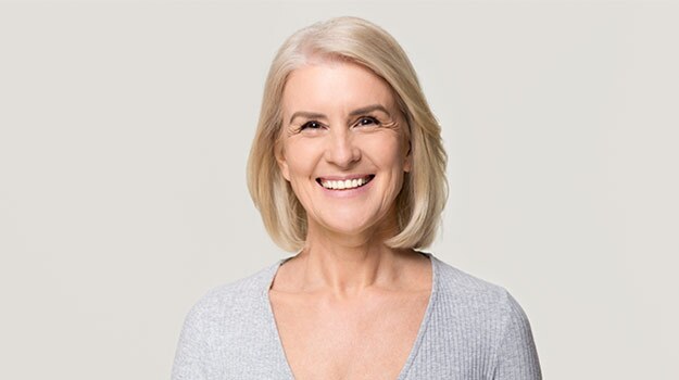 A smiling senior Caucasian woman with short blonde hair, wearing a gray sweater, representing successful periodontal surgery recovery in Sandpoint, ID.