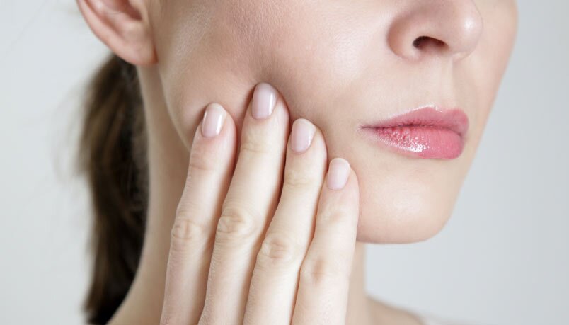 Close-up of a woman gently touching her jaw, indicative of TMJ discomfort, highlighting TMJ treatment in Sandpoint, Idaho.