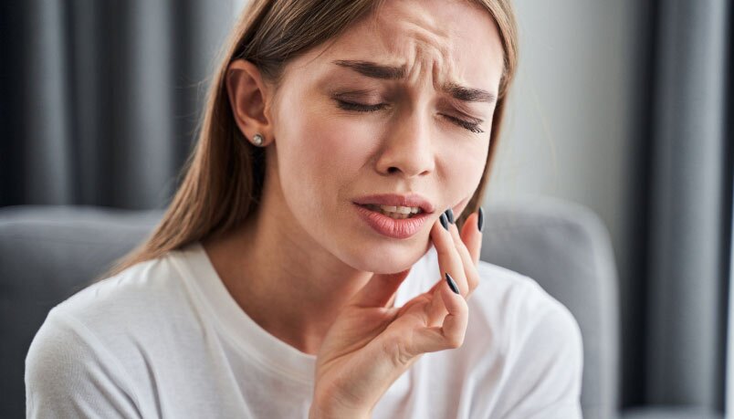 A young woman in distress due to a toothache, highlighting the need for emergency dentistry services in Sandpoint.