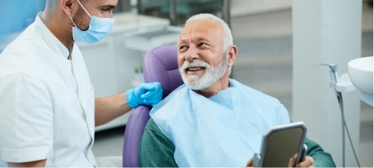 an old man sitting in a dental chair and smiling at a dentist in Sandpoint, Idaho clinic, likely discussing free dental implant consultations.