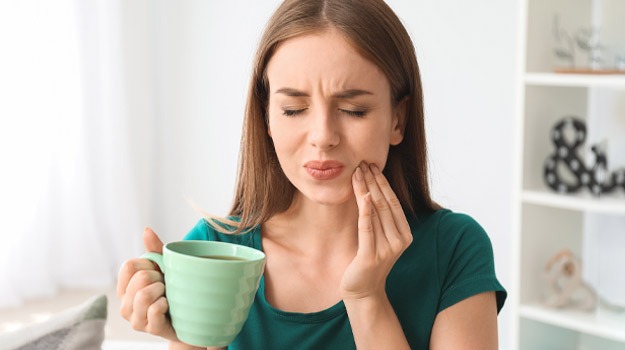A woman in green wincing in pain, possibly needing tooth extractions in Sandpoint, Idaho.