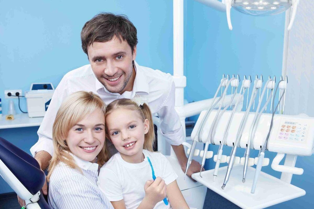 Family dentist with smiling parent and child during a dental visit in a modern dental office