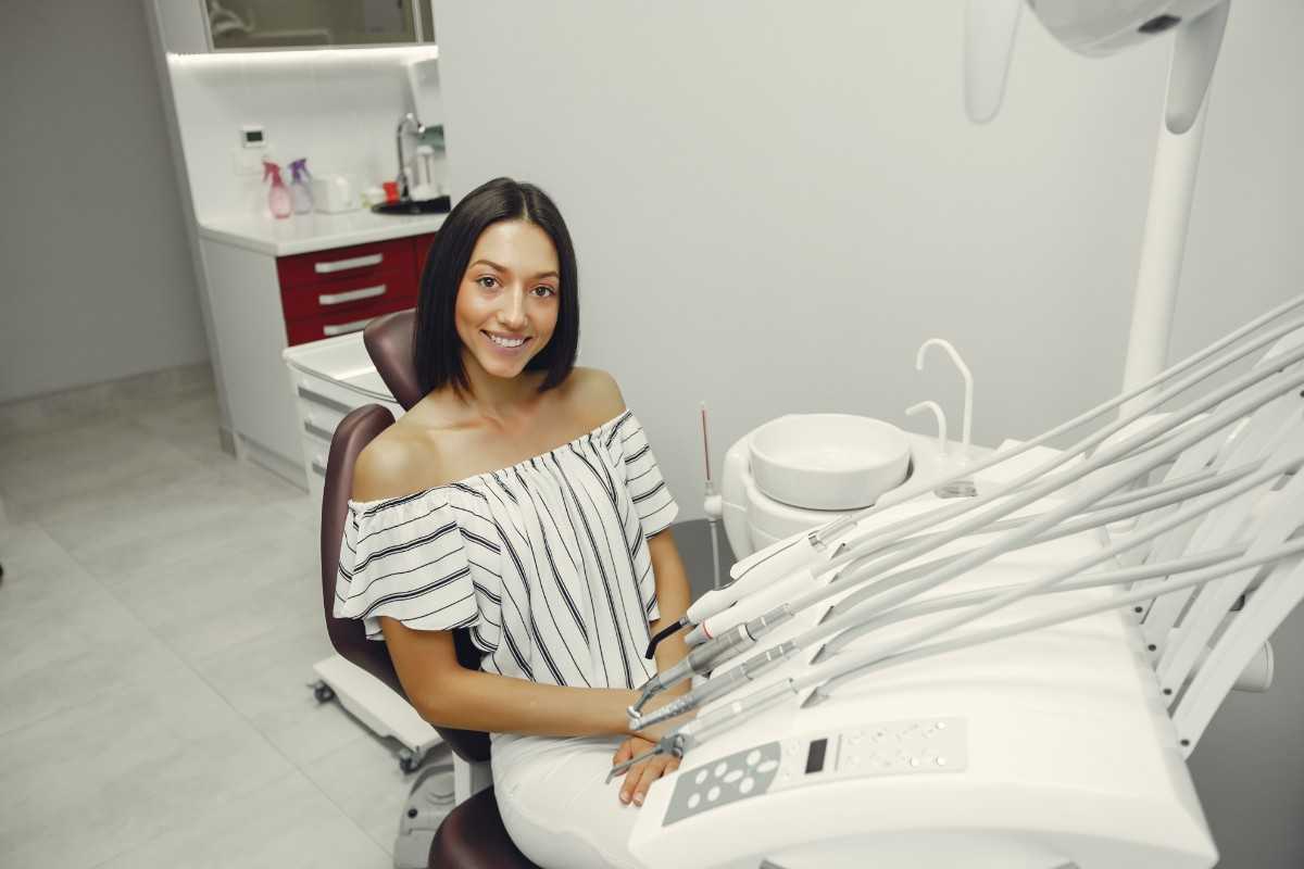 A woman in a dental chair, looking anxious, with her hands on her head during a dental appointment.